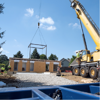 Crane placing a prefabricated building into place. construction workers are around the building.  