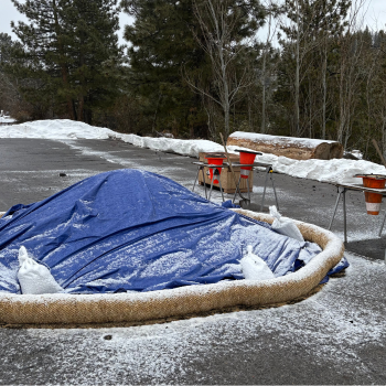 Photo of a sand pile covered in a tarp with a dusting of snow. 