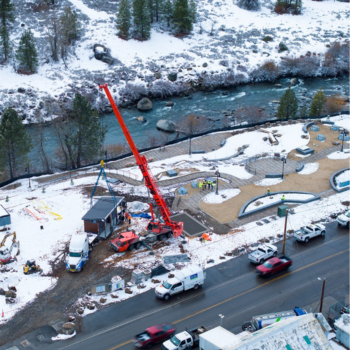 Restrooms being installed by large crane at a park along a river with snow surrounding it. 