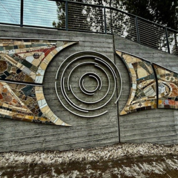 A retaining wall on the street with a large, swirling, sculptured art piece on it.