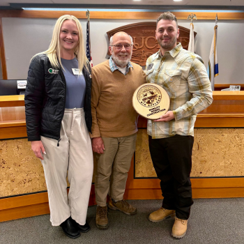 A man and women stand with Mayor Jan Zabriskie in Council Chambers to accept award. 