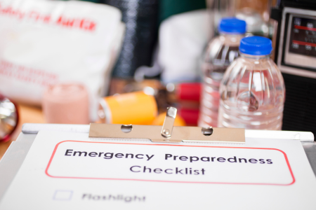 A clipboard with an Emergency Preparedness Checklist shown and supplies around it. 