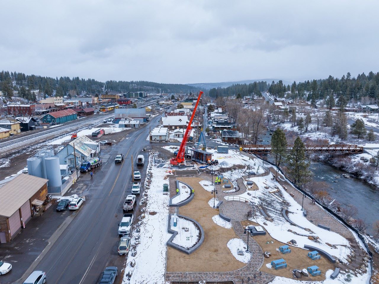 Restrooms being installed by large crane at a park along a river with snow surrounding it. 